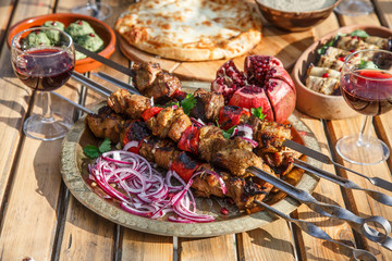 Meat shish kebab on a plate with onions, pomegranate seeds, hot pepper, wooden backdrop background