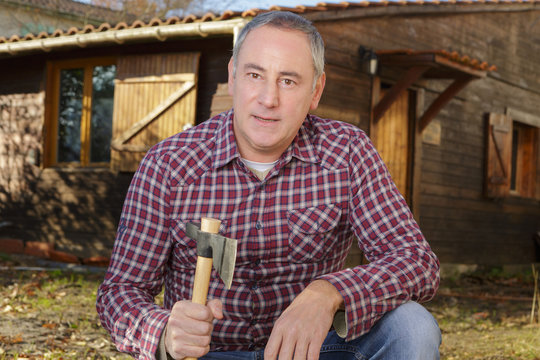 man standing near old wooden house and holding axe