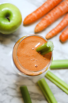 Fresh carrot juice in a glass with celery stalks, carrots and an apple. Top view.