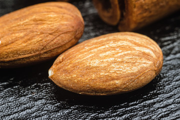 Yellow raw almond nuts kernel on black leather texture background, macro image