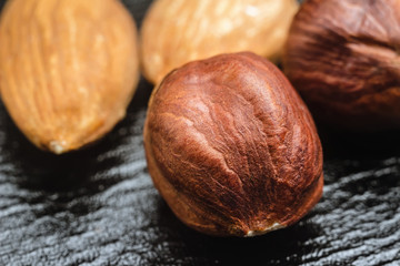 Brown, raw hazelnut kernel and almond nuts on black leather texture background, macro image