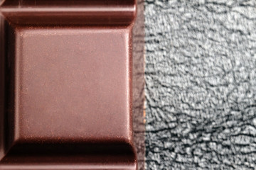 Dark, bitter chocolate in cubes shape on black leather texture background, top view