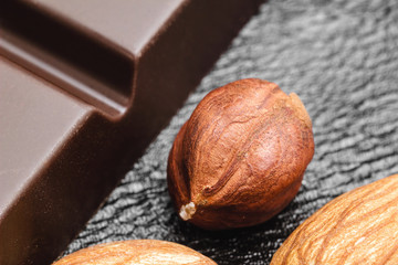 Raw brown kernel of hazelnut and dark bitter chocolate on black leather texture background, macro...