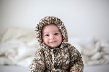 Little baby boy playing at home in bed, dressed in hand made knitted overall