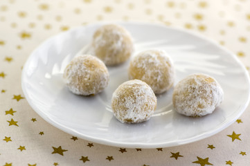 Christmas cookies, tasty balls with hazelnut inside and icing sugar, white plate and tablecloth with golden stars