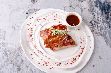 Top view of American food barbecue ribs steak with pepper sauce ketchup in ceramic dish on white plate, on gray concrete background. restaurant kitchen concept