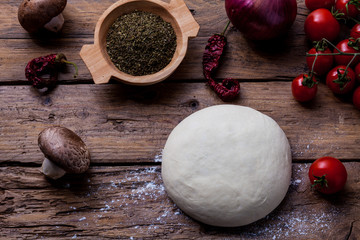 Pizza dough with ingredients on wood board