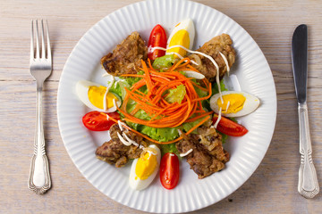 Liver salad with carrot, eggs, tomatoes and lettuce on white plate