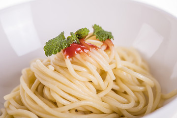 close up of cooked shpaghetti in a white bowl with tomato sauce and herb leave on top 
