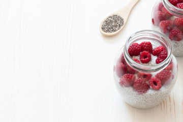 Glass Jar with pudding from chia seeds with coconut milk and raspberry berries on white wooden table. Simple breakfast. Concept of a healthy diet.