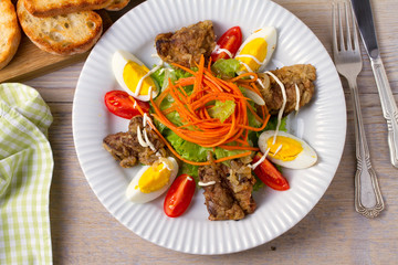 Liver salad with carrot, eggs, tomatoes and lettuce on white plate