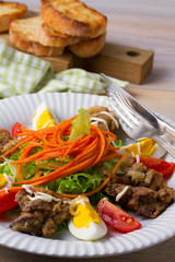 Liver salad with carrot, eggs, tomatoes and lettuce on white plate