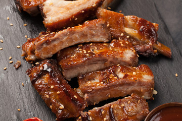 Pork ribs in barbecue sauce and honey roasted tomatoes on a black slate dish. A great snack to beer on a black stone background. Top view