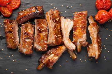 Pork ribs in barbecue sauce and honey roasted tomatoes on a black slate dish. A great snack to beer on a light stone table. Top view