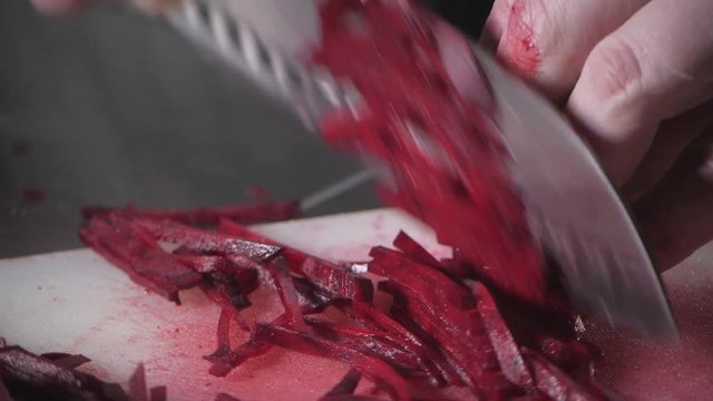 Closeup of hand with knife cutting fresh vegetable. Young chef cutting beet on a white cutting board closeup. Cooking in a restaurant kitchen