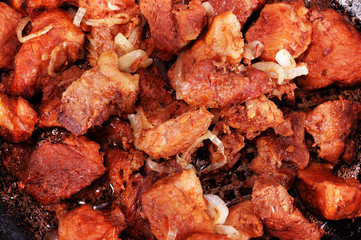 Close-up of roasted meat slices with sliced onion and sauce on the frying pan