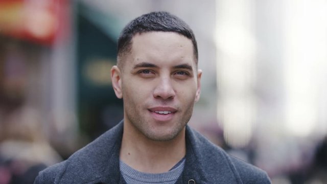 Portrait of handsome mixed race male smiling to camera in a busy high street, in slow motion