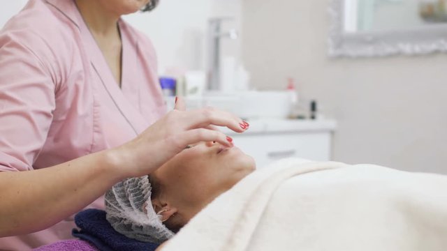 Beautician applies protective balm on patient's lips before facial massage
