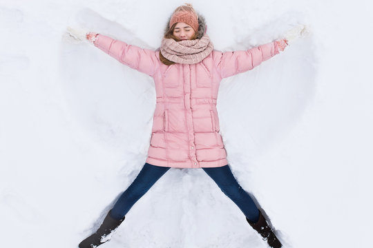 happy woman lying in the snow and moving arms and legs up and down, creating the shape of a snow angel. Smiling woman lying on snow in winter holiday ,for advertising ,