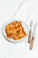Traditional German or Austrian Wiener Schnitzel or Schnitzel Wiener Art made of breaded and pan-fried butterfly cutlet of pork, veal of chicken meat on white wooden background