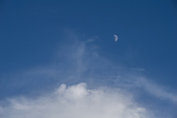 The moon out in the middle of the day and white fluffy clouds