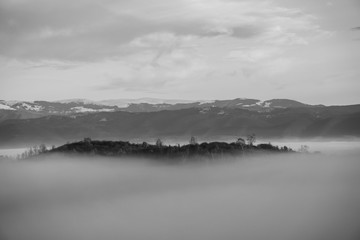 Black and white shot of small hill piercing the thick fog that engulfed the valley below