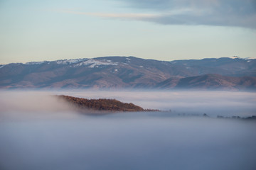 Waves of fog engulf the valley below while a small hilltop creates an island in the misty sea