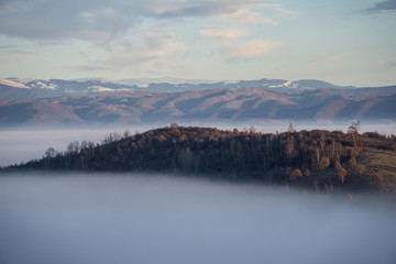 Beautiful landscape in the foothills of the Carpathian mountains with fog rolling in and a hill rising in the middle of the valley