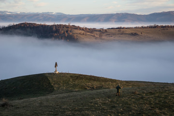 A lonely shepard makes his way downhill as thick for engulfs the valley below