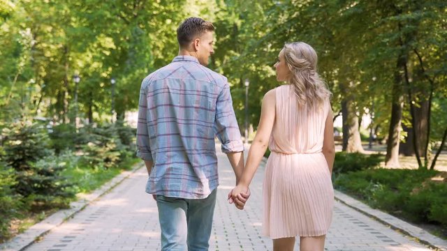 Couple in love strolling through beautiful summer park, gently holding hands