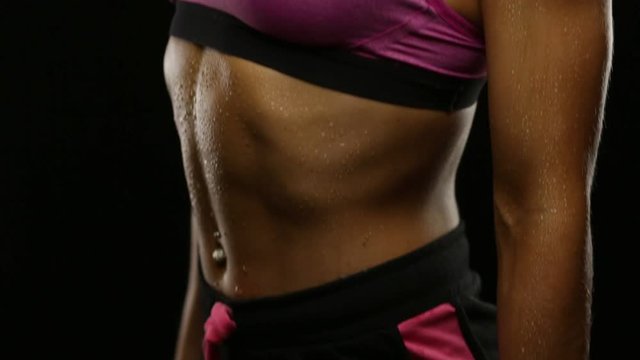 Body with water drops of young fit woman with dumbbells posing on black. Vertical panning. Seamless loop