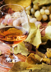Brandy in a glass and fresh grapes with leaves and a vine, still life in rustic style, vintage wooden background, selective focus