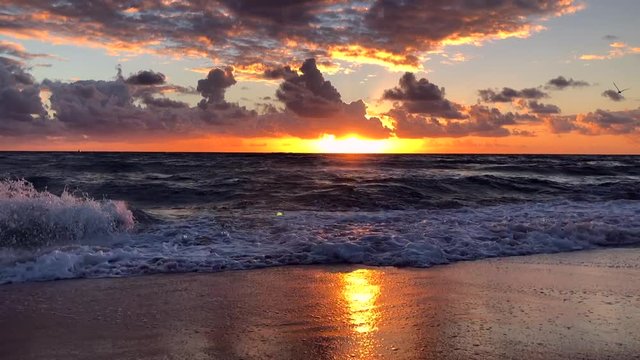 Waves crashing in slow motion in front of a golden sunrise sky in Miami, Florida