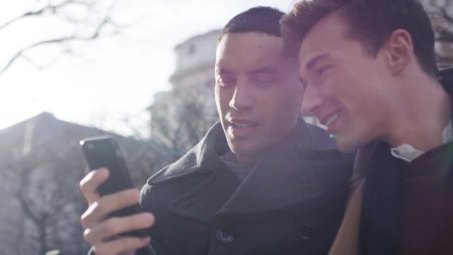 Young male couple laugh at something on a phone and share a kiss