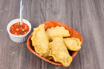 Colombian empanada with spicy sauce on wooden background