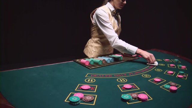 Casino croupier girl distributes cards on the poker table top using cut card. Black background. Slow motion