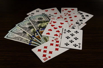 Playing cards and one hundred dollar bills on a dark wooden table