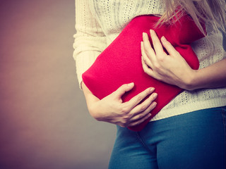 Woman feeling stomach cramps holding hot water bottle