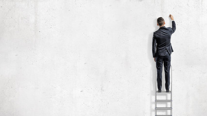 A businessman stands on a step ladder in a back view and draws on an empty white wall.