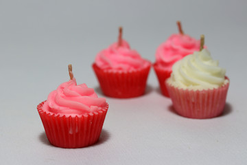 Pink candle in cupcake shape with out focus three candle put on light grey background. it is a wax with a central wick that is lit to produce light as it burns.