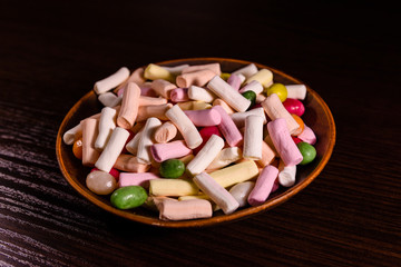 Ceramic dish with the different multi colored candies on a dark wooden table