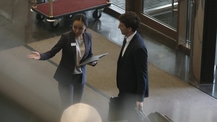 High angle view of businessman walking into hotel with luggage; Asian hotel worker meeting and greeting him in lobby