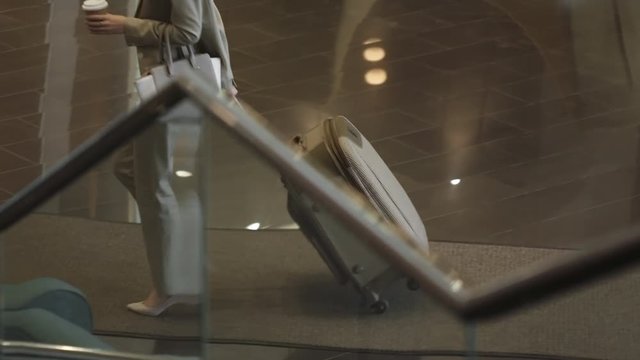 Panning shot of businesswoman walking through hotel lobby with luggage and coffee cup