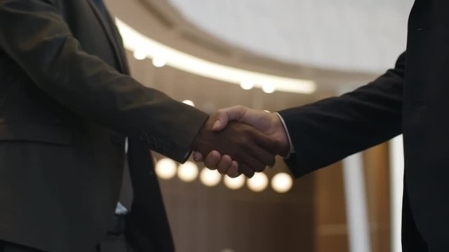 Closeup panning shot of handshake of African and Caucasian business partners in hotel lobby