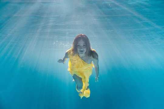underwater picture of beautiful young woman in dress swimming in swimming pool