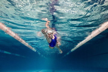 underwater picture of female swimmer in swimming suit and goggles training in swimming pool - obrazy, fototapety, plakaty