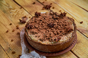 Fototapeta na wymiar Homemade cheesecake with chocolate powder on the brown plate decorated with white cloth, silver spoon and raisins. Delicious chocolate tart with anise stars on the wooden background. Side view
