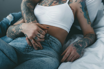 cropped view of tattooed couple holding hands and relaxing on bed