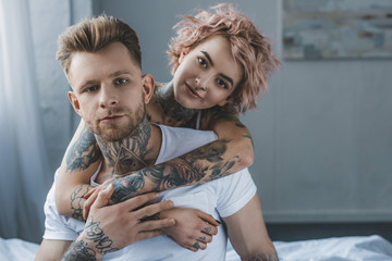smiling tattooed girl hugging her boyfriend on bed in bedroom