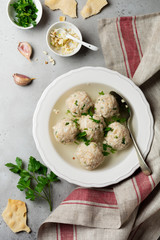Homemade chicken matzo ball soup with parsley and garlic in simple white ceramic plate on a gray stone or concrete background.  Traditional Jewish passover dish. Selective focus. Top view.